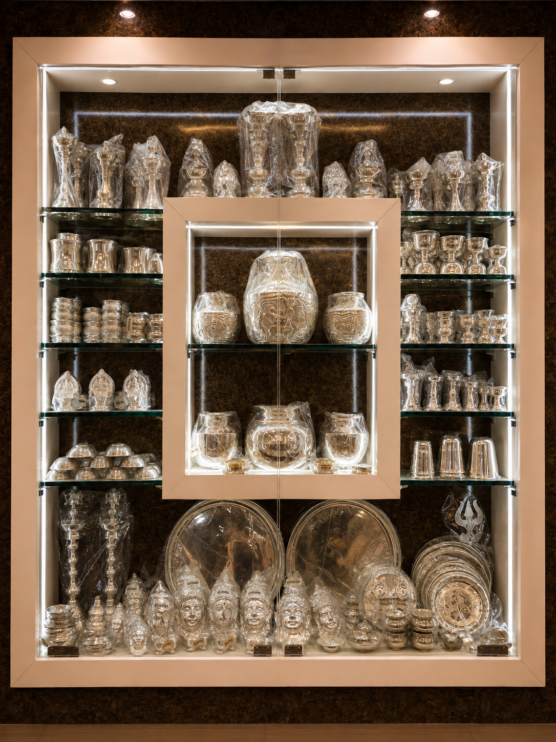 Silver pooja articles and utensils on lit glass shelves